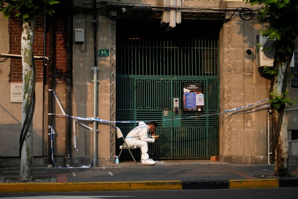 A worker in a protective suit eats dinner at a closed residential area during lockdown, amid the Covid-19 pandemic, in Shanghai, China May 16, 2022. — Reuters pic