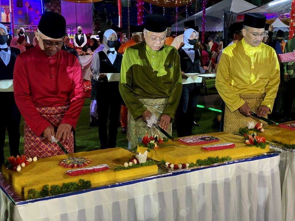 Prime Minister Datuk Seri Ismail Sabri Yaakob (centre) with Senior Defense Minister Datuk Seri Hishammuddin Hussein (right) and Chief of Army Staff General Tan Sri Affendi Buang (left) cutting yellow glutinous rice cakes during the Hari Raya Aidilfitri Open House of the Malaysian Army at Kem Perdana in Sungai Besi, May 21, 2022. — Bernama pic
