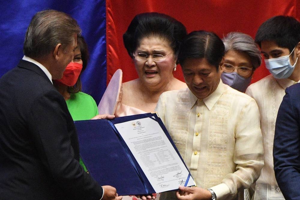 Philippine President-elect Ferdinand Marcos Jr poses with his certificate of proclamation as the country's president with Senate President Vicente Sotto III, as family members including his mother and former first lady Imelda Marcos look on at the House of Representatives in Quezon City, suburban Manila May 25, 2022. — AFP pic