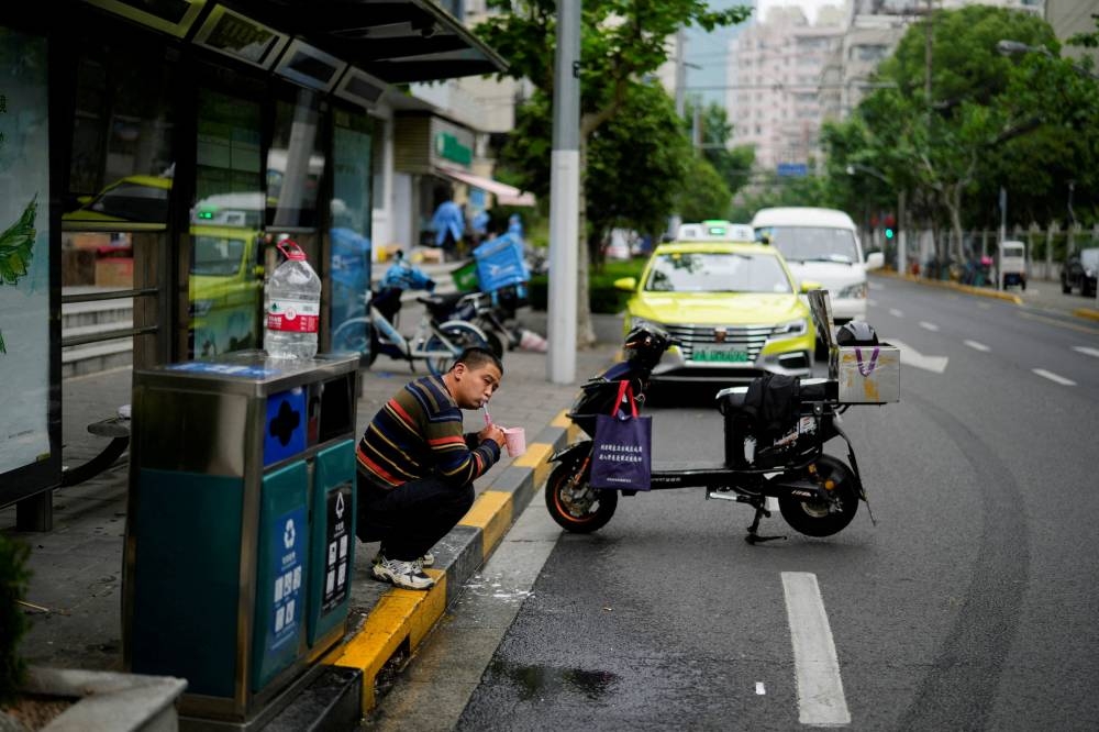 A delivery worker, who says he is living at a bus stop because he has been unable to return home for weeks due to the lockdown, brushes his teeth on a street, amid the Covid-19 pandemic, in Shanghai May 12, 2022. — Reuters pic
