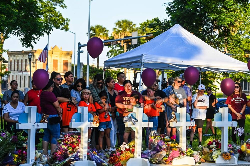 Soccer teammates of Tess Mata, who died in the shooting, cry, supported by their mothers, as they visit a makeshift memorial outside the Uvalde County Courthouse in Texas on May 26, 2022.— AFP pic