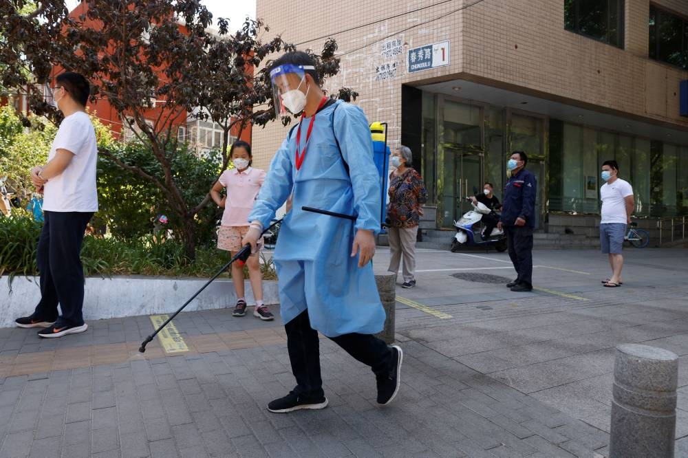 A worker wearing personal protective equipment sprays disinfectant next to people lining up to get tested at a makeshift nucleic acid testing site amid the Covid-19 outbreak in Beijing, China May 27, 2022. — Reuters pic