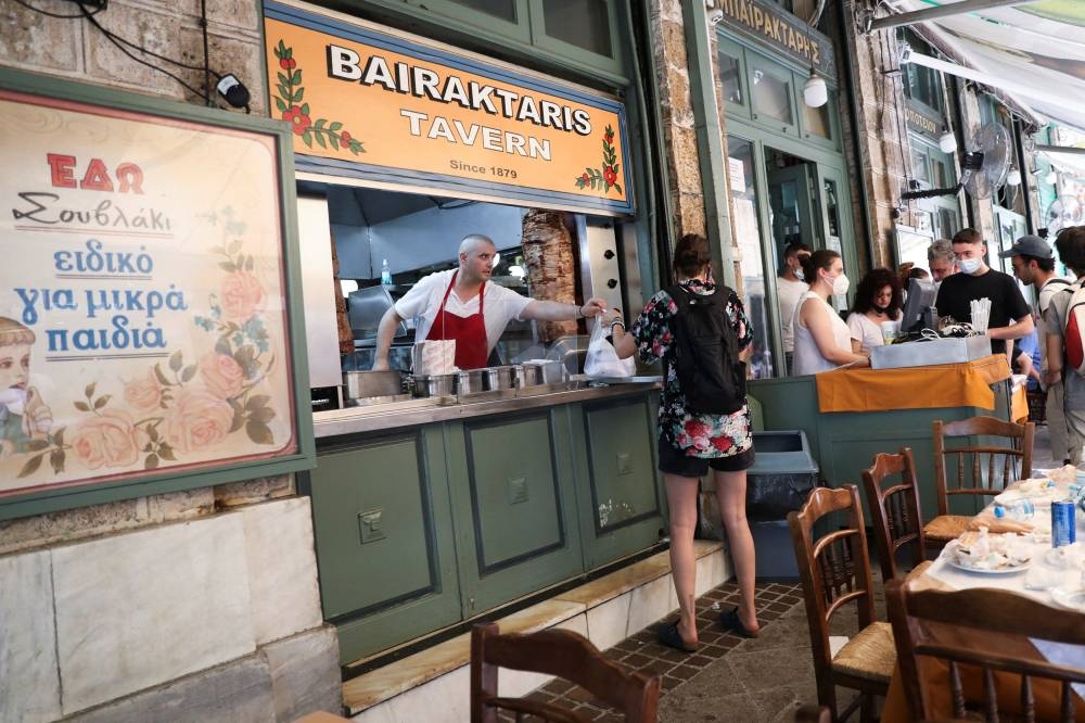 A cook gives a customer a souvlaki, a popular Greek fast food made with pieces of meat grilled on a skewer, in a restaurant, in Athens May 27, 2022. — Reuters pic