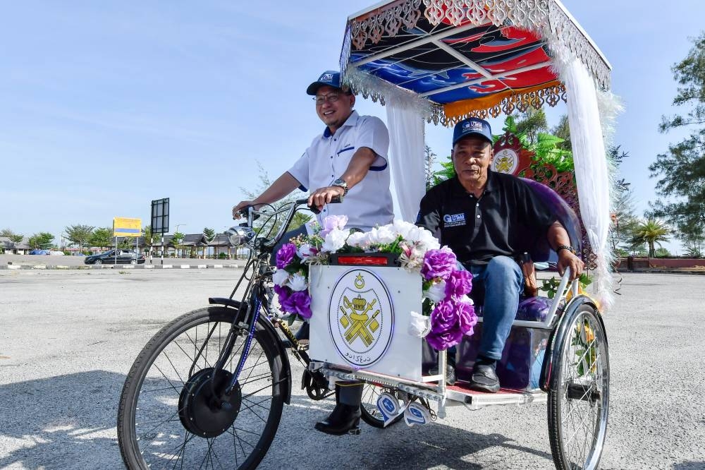 Deputy Minister Datuk Ahmad Amzad Hashim (left) tries out an electric trishaw (e-BECA) made by Universiti Teknikal Malaysia Melaka (UTeM) durnig the Aspirasi Keluarga Malaysia (AKM) Tour in Kuala Terengganu June 2, 2022. — Bernama pic