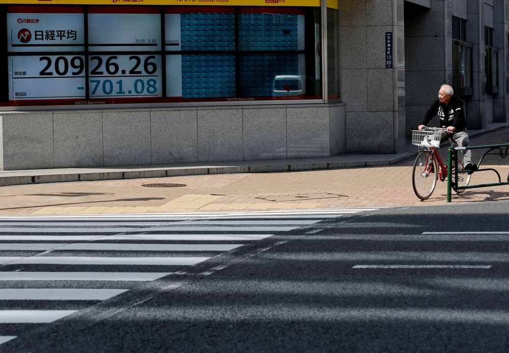 A man in a bicycle stops in front of an electronic board showing the Nikkei stock index outside a brokerage in Tokyo, Japan. ― Reuters pic