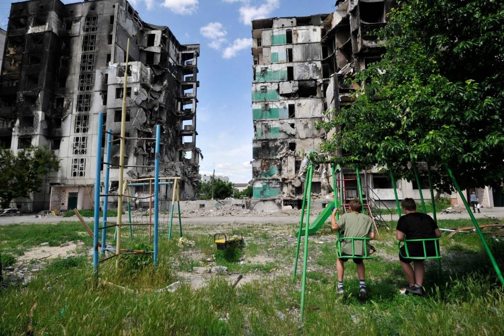 Two boys sit on swings on a playground in front of a destroyed residential building in the town of Borodyanka on June 7, 2022, amid the Russian invasion of Ukraine. — AFP pic
