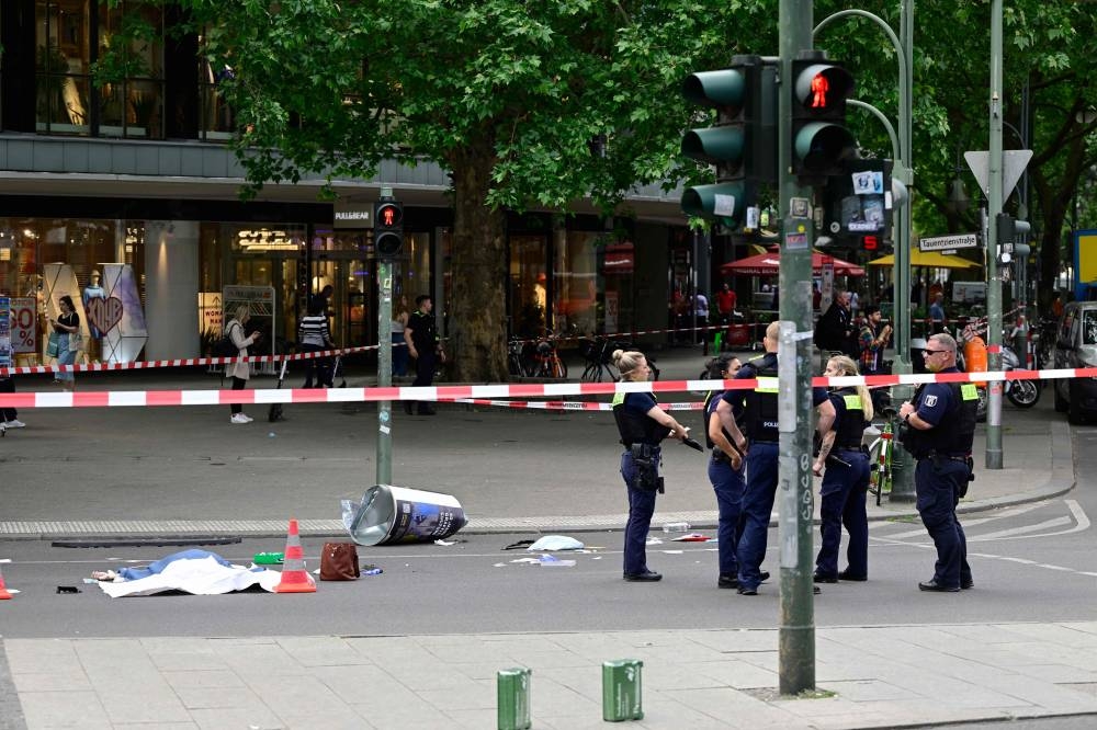 Police stand near the body of a dead person at a cordoned-off area where a car ploughed into a crowd near Tauentzienstrasse in central Berlin, on June 8, 2022. — AFP pic