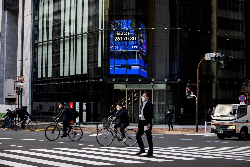 People cross a road near an electronic quotation board displaying closing numbers of the Nikkei 225 index of the Tokyo Stock Exchange in Tokyo, January 27, 2022. — AFP pic 
