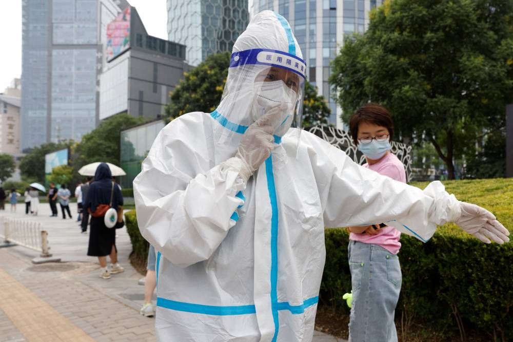 A worker wearing PPE walks next to people lining up to get tested at a mobile nucleic acid testing site amid the Covid-19  outbreak in Beijing, China June 10, 2022. — Reuters pic