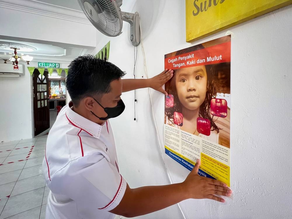 A health worker puts up a poster on the hand, foot and mouth disease (HFMD) at a kindergarten in Labuan June 8, 2022. — Bernama pic