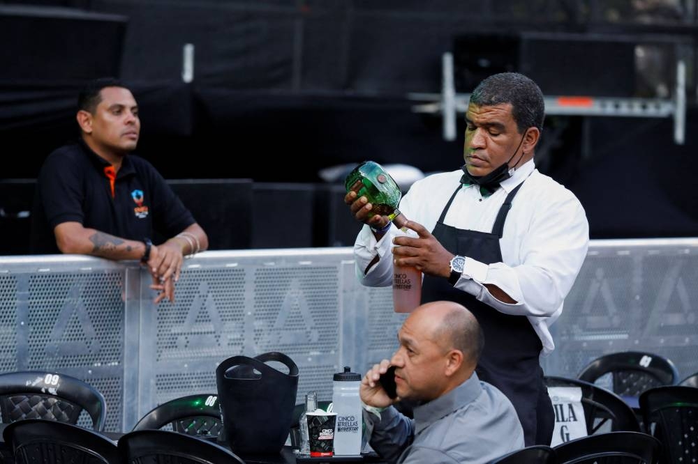 A waiter serves a Whiskey bottle in a plastic thermos in the VIP area during an urban music festival housed in the open parking lot of a shopping centre in Caracas, Venezuela June 4, 2022. — Reuters pic