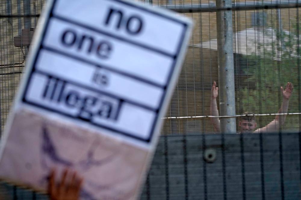 Protesters communicate with those inside at the perimeter fence of Brook House immigration removal centre beside Gatwick Airport, south of London on June 12, 2022, as demonstrators gather to protest against the UK government's intention to deport asylum-seekers to Rwanda. — AFP pic