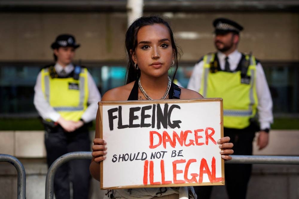 A protester holds a placard as she stands outside the Home Office in central London on June 13, 2022, to demonstrate against the UK government's intention to deport asylum-seekers to Rwanda. — AFP pic