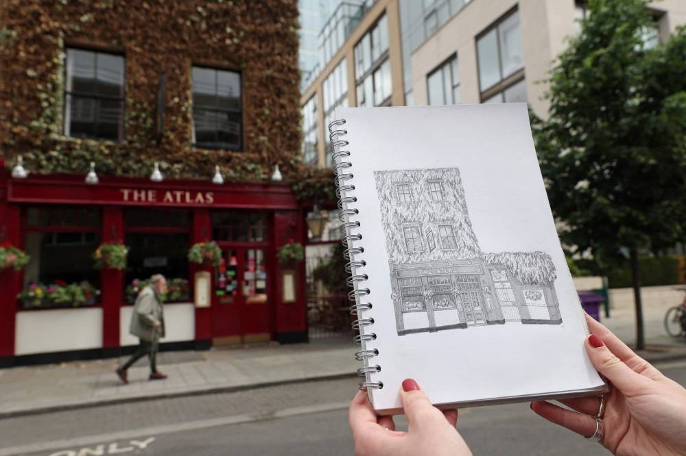 Artist Lydia Wood holds up her finished drawing of The Atlas pub in west London on May 26, 2022. — AFP pic