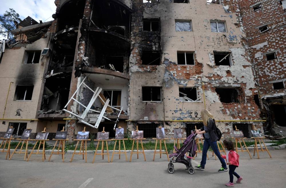 A woman and her daughter walk past a residential building destroyed as a result of shelling in town of Irpin, near  the Ukrainian capital of Kyiv June 16, 2022. — AFP pic