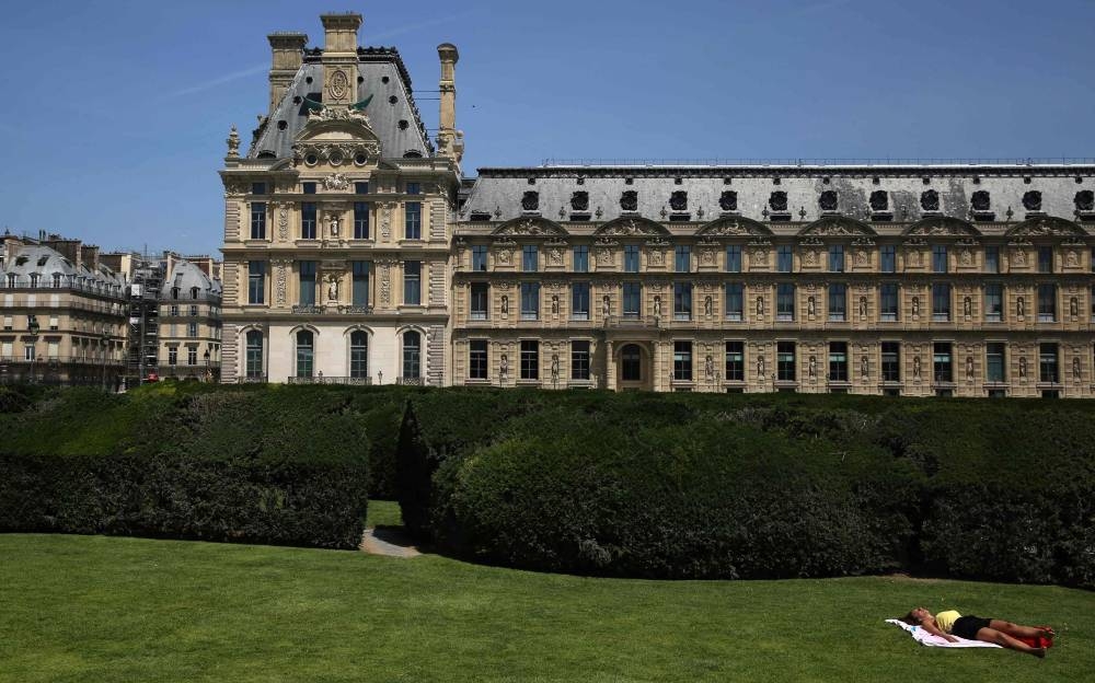 A sunbather lies on grass in front of The Louvre Museum in Paris on June 17, 2022, as a heatwave sweeps across much of France and Europe. ― AFP pic