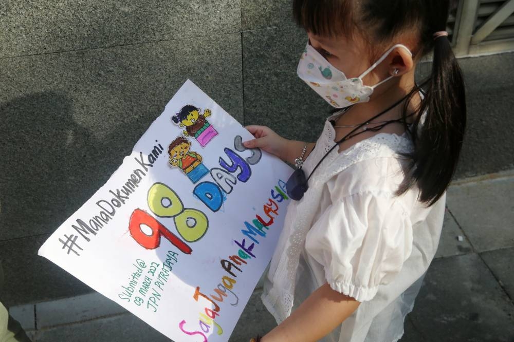 Lin Peak Yee's daughter holds a poster asking for her citizenship papers at the National Registration Department headquarters in Putrajaya on June 10, 2022. — Picture by Choo Choy May