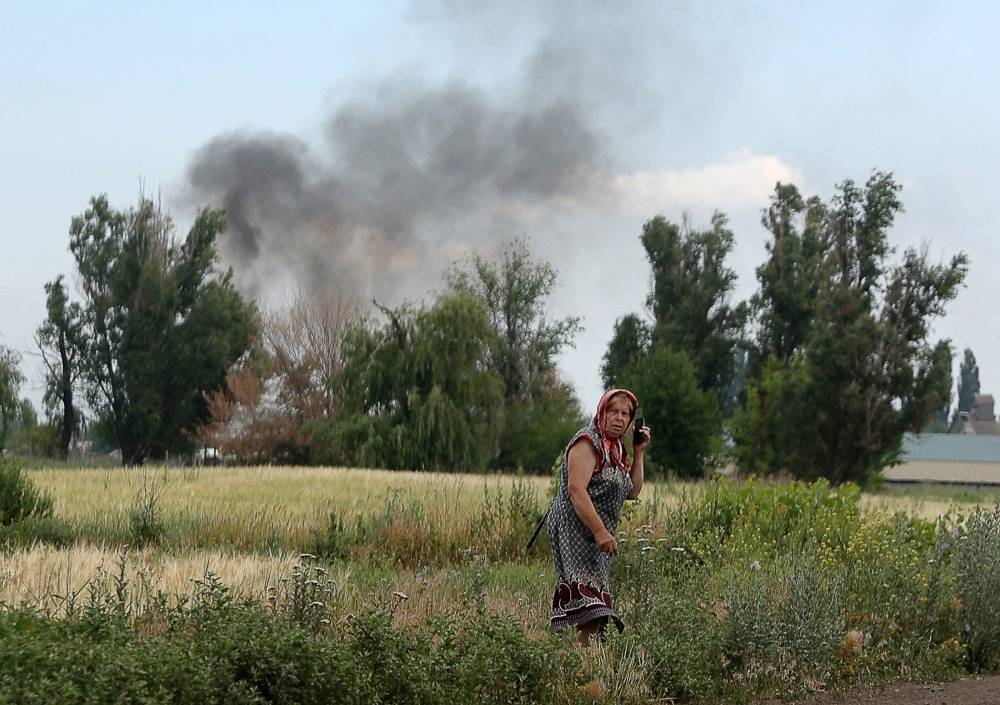 A woman speaks on a mobile phone on a roadside while smoke rises behind in the village Sviato-Pokrovske, Donetsk region, on June 23, 2022, amid Russia’s military invasion launched on Ukraine. — AFP pic