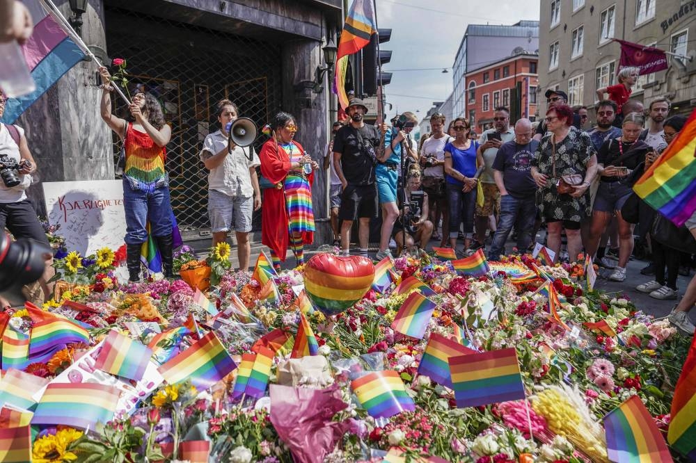 People with Pride flags stand near the London pub and lay flowers on June 25, 2022, in the aftermath of a shooting outside pubs and nightclubs in central Oslo killing two people injuring 21. — AFP pic 