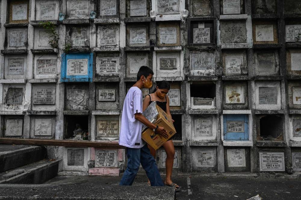 This photo taken on June 10, 2022 shows relatives of a victim of the government's drug war carrying a box containing the remains after they were exhumed at Bagbag Cemetery in Novaliches, Metro Manila. — AFP pic