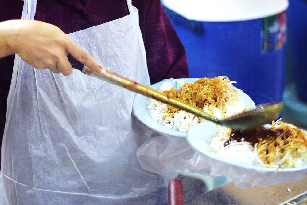 Ladling different curries ('kari campur') for takeaway orders.