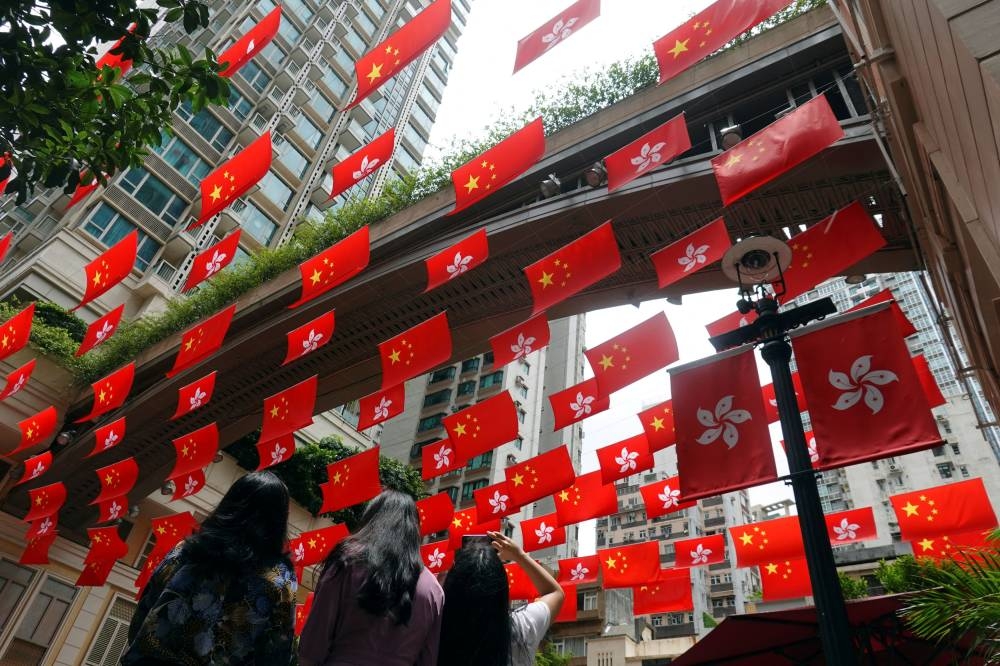 A woman takes pictures of Chinese and Hong Kong flags decorating a street, ahead of the 25th anniversary of the former British colony's handover to Chinese rule, in Hong Kong June 30, 2022. ― Reuters pic