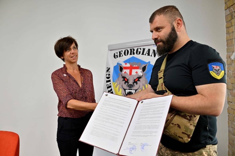 Marie Lequin (left), head of Geneva Call Eurasia region, and the head of the Georgian National Legion Mamuka Mamulashvili shake hands and hold a signed agreement to observe international norms after a presentation organised by a Swiss NGO called Geneva Call in Kyiv on June 30, 2022 as a part of its efforts to meet and provide guidance to a wide range of Ukrainian combatants. ― AFP pic