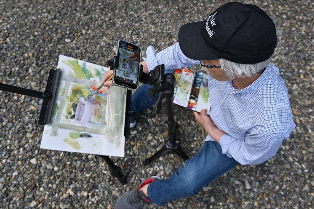 This picture taken on May 25, 2022 shows Japanese art instructor Harumichi Shibasaki painting with watercolours while recording video footage using his phone at a shrine in Isumi, Chiba prefecture. — AFP pic