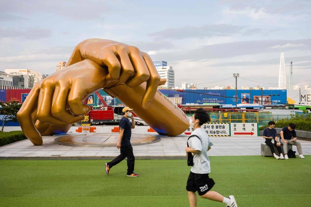 A man runs past a bronze sculpture by artist Hwang Man-seok, modelled after the signature horse-riding hand motion of the ‘Gangnam Style’ song, in the Gangnam district of Seoul, July 15, 2022. — AFP pic 