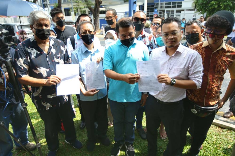 PKR deputy president Rafizi Ramli (centre) holds up a copy of the police report against Datuk Seri Najib Razak at the Setiawangsa police station July 19, 2022. — Picture by Ahmad Zamzahuri