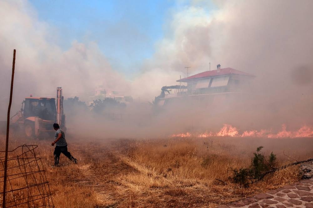 A person runs as wildfire approaches houses on Vatera coastal resort on the eastern island of Lesbos on July 23, 2022. - Residents were evacuated as the wildfire threatened properties. ― AFP pic
