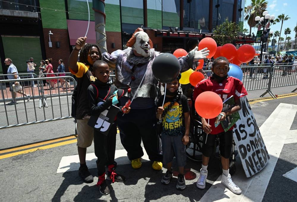 People pose for a photo with a cosplayer dressed as a scary clown in the Gaslamp District outside Comic-Con International in San Diego, California, on July 23, 2022. — AFP pic
