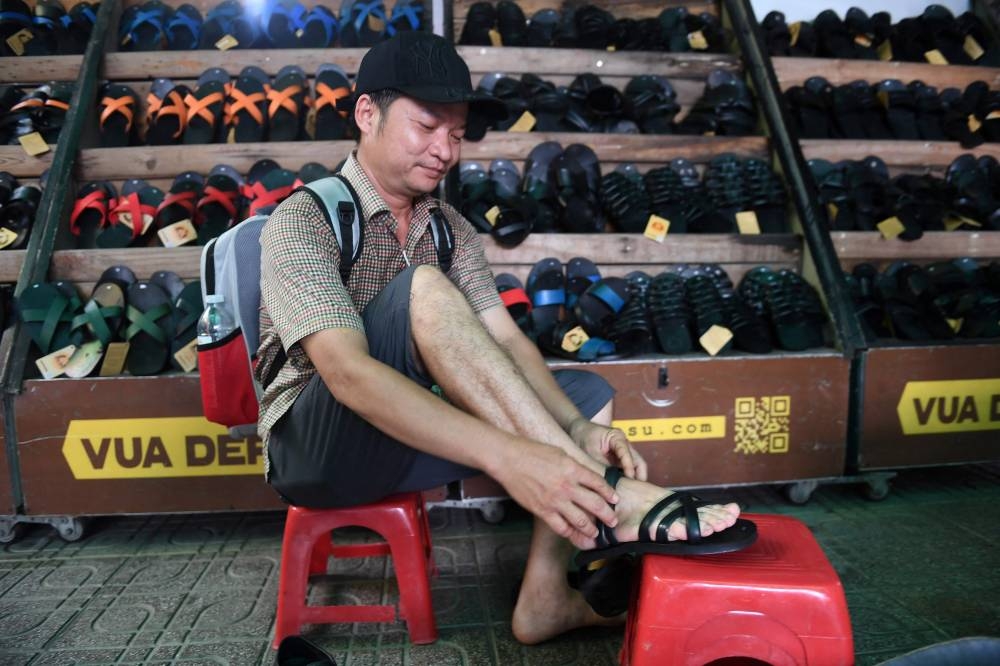 This photo taken on July 5, 2022 shows a client trying on rubber sandals at a shop in Hanoi. — AFP pic