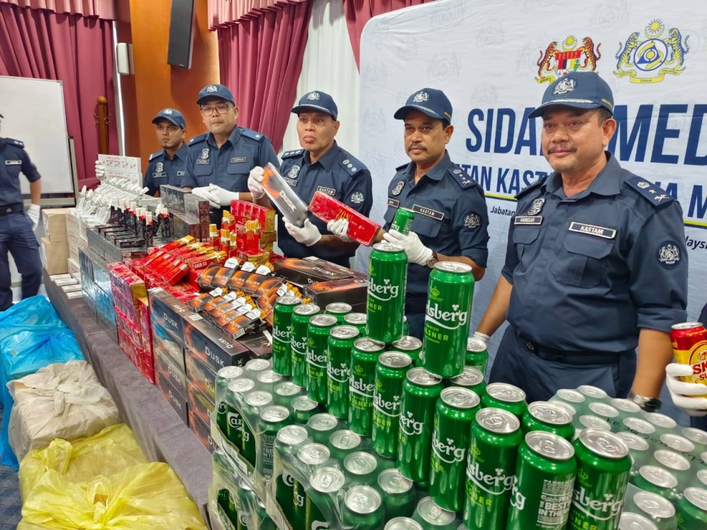 Johor Customs Department officers with the confiscated contraband cigarettes and beer during the media conference at Menara Kastam Johor in Johor Baru today. Aug 3, 2022. — Picture by Ben Tan