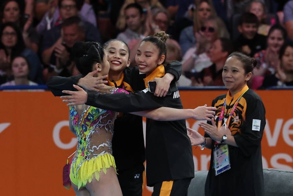 National gymnast Ng Joe Ee (right) is hugged by teammates Izzah Amzan and Koi Sie Yan after the rhythmic gymnastics 'Ribbon' final event in conjunction with the Birmingham 2022 Commonwealth Games at the Birmingham Arena August 6, 2022. Ng Joe Ee won the country's sixth gold medal after scoring the highest score of 27.800. — Bernama pic