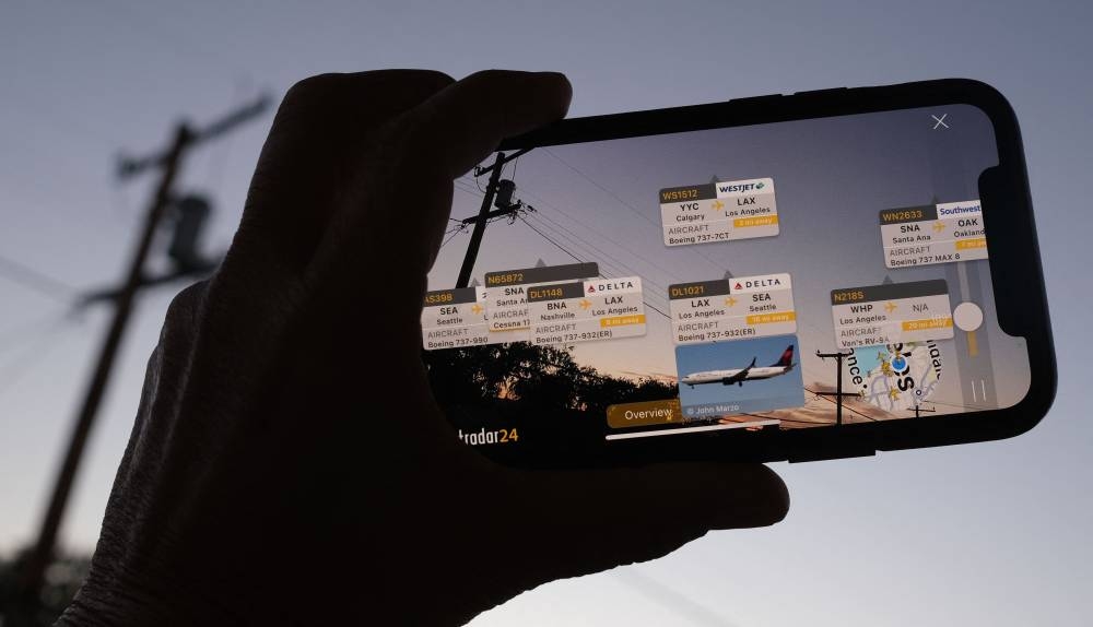 In this illustration photo, the Flightradar24 app is seen on a smartphone in front of a screen showing the live position of planes tracked by the app in the area of Los Angeles, California, on August 5, 2022. — AFP pic