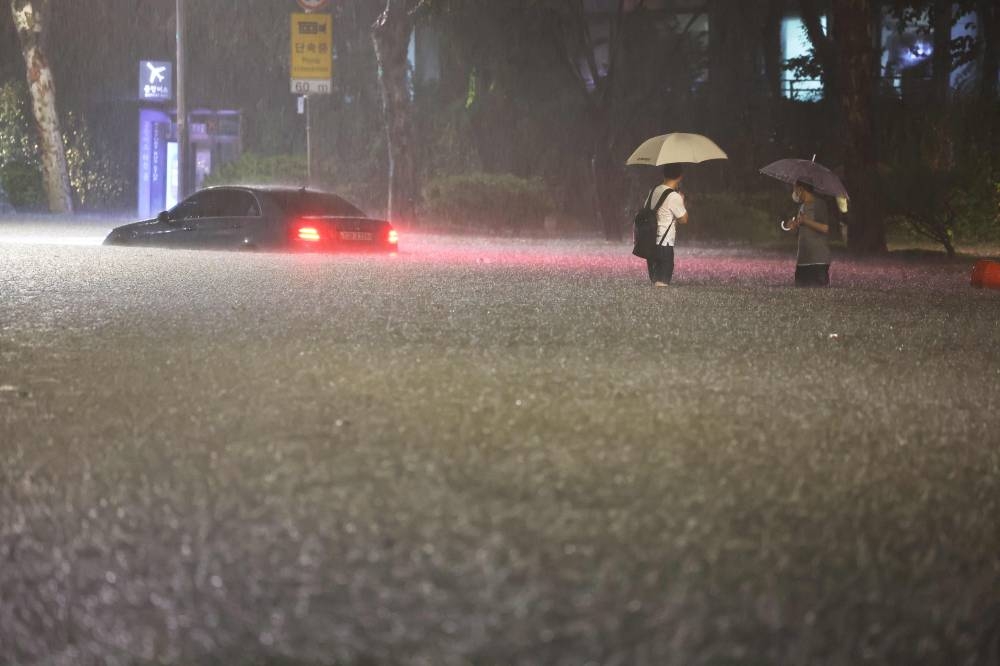 People wade alongside submerged cars in a street during heavy rainfall in the Gangnam district of Seoul on August 8, 2022. ― AFP pic