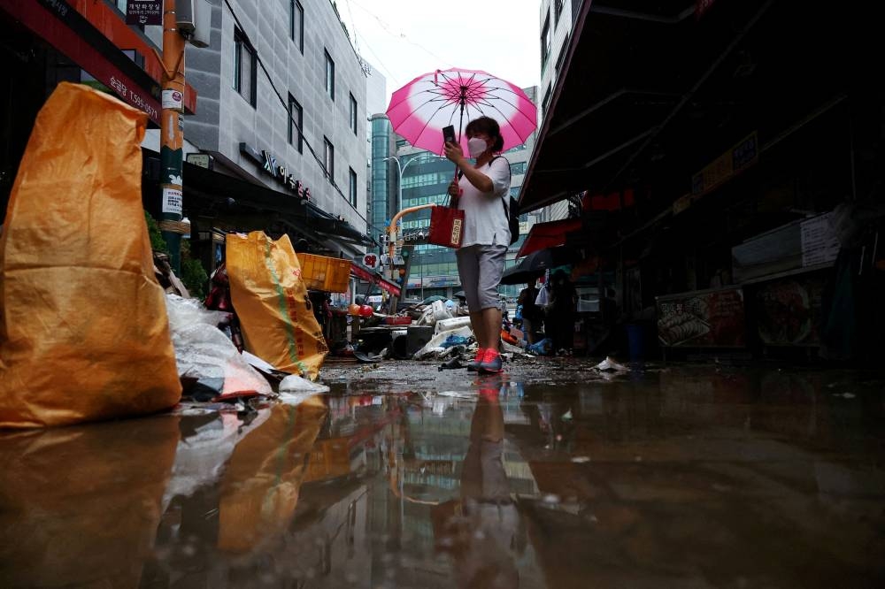 A woman using an umbrella takes photographs of a road that was flooded after torrential rain, at a traditional market in Seoul, South Korea August 9, 2022. ― Reuters pic