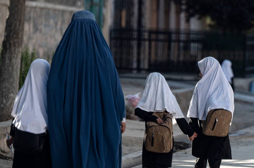 An Afghan woman walks with schoolgirls going to their primary school in Kabul August 9, 2022. — AFP pic