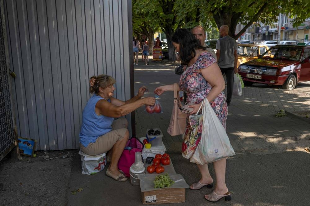 A women buys tomatoes from a street vendor in the Ukrainian city of Marhanets, on August 12, 2022 amid the Russian invasion of Ukraine. — AFP pic