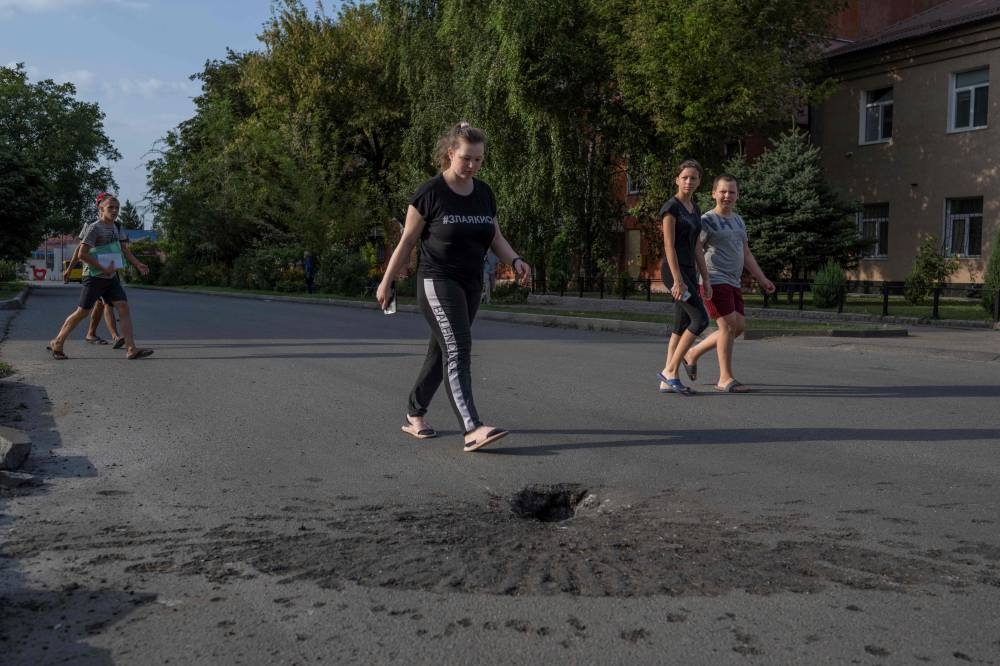 People walk next to a crater left by a shelling by Russian forces in the Ukrainian city of Marhanets, on August 12, 2022 amid the Russian invasion of Ukraine. — AFP pic