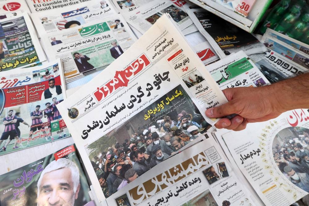 A man shows today’s edition of the Iranian newspapers, Vatan-e Emrooz, with the front page title reading in Farsi: ‘Knife in the neck of Salman Rushdie’, in the capital Tehran on August 13, 2022, a day after a man stabbed British author Salman Rushdie, the target of a 1989 Iranian fatwa calling for his death, during a literary event in New York state. — AFP pic