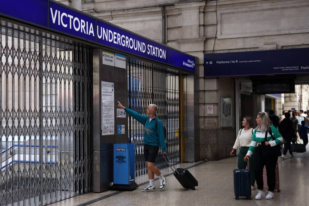 Passengers study an information sheet displayed outside Victoria Underground Station London, on August 19, 2022, advising the public on strike action on Buses, National Rail and London Underground. — AFP pic