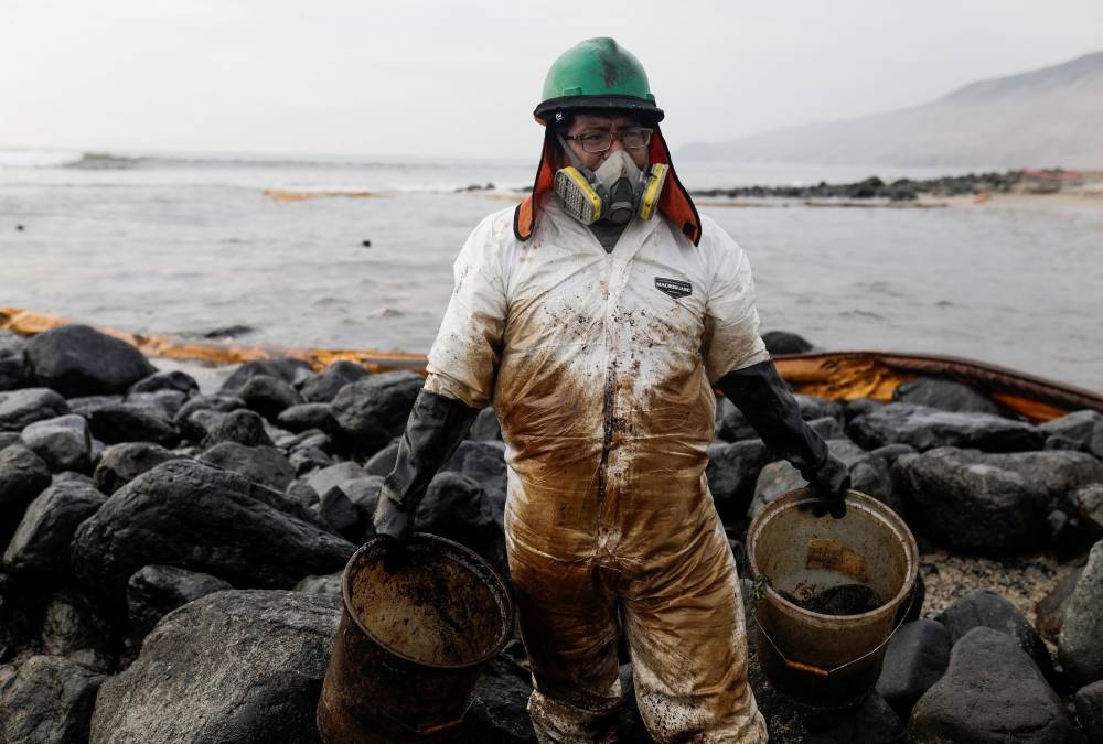 A worker cleans up an oil spill at the beach as demonstrators take part in a protest outside Repsol's La Pampilla refinery against the recent oil spill that has caused an ecological disaster on the coasts of Lima, in Ventanilla, Peru January 29, 2022. — Reuters pic