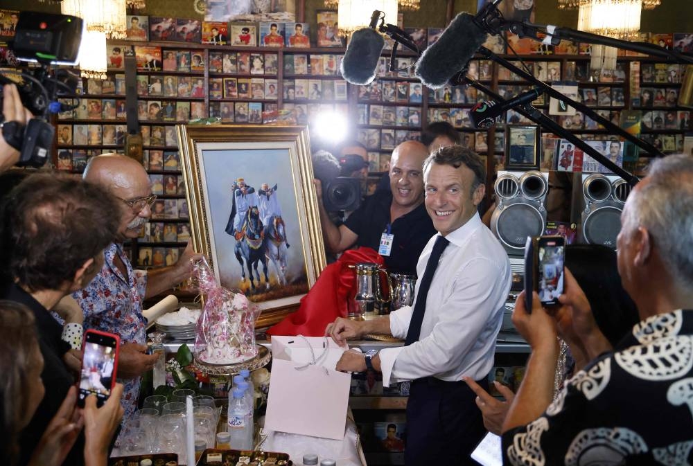 France’s President Emmanuel Macron (centre) receives a gift from Boualem Benhaoua (2nd left), owner of the disco Maghreb Shopin, mythical label of rai music, during his visit in Oran on August 27, 2022. — AFP pic