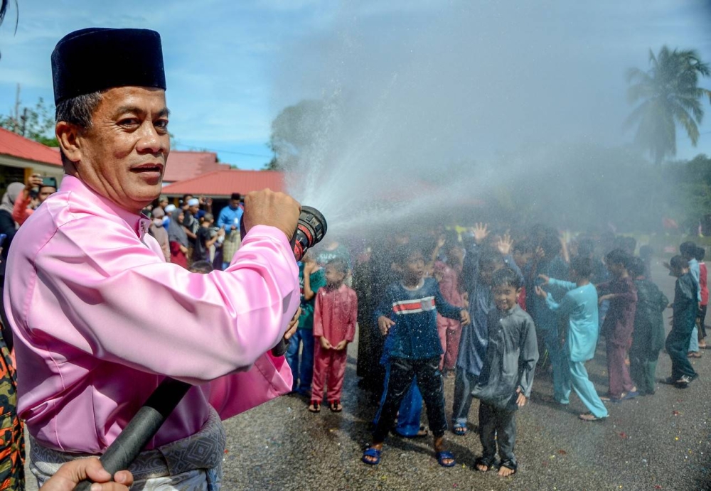 Kelantan state health director Datuk Dr Zaini Hussin spraying water at children participating in the 2022 Alor Pasir Charity Sunathon program at the Al-Mustaqim Alor Pasir Mosque in Tanah Merah, September 3, 2022. — Bernama pic