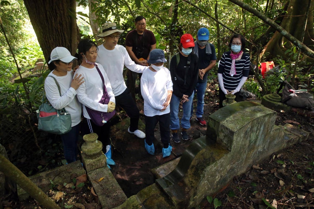 Mr Winston Teo and his family paying a visit to his grandfather’s grave in Kopi Sua (Coffee Hill) near Bukit Brown on June 19, 2022. They were accompanied by Mr Peter Pak (at back, in maroon top), who helped Mr Teo locate the grave. — TODAY pic