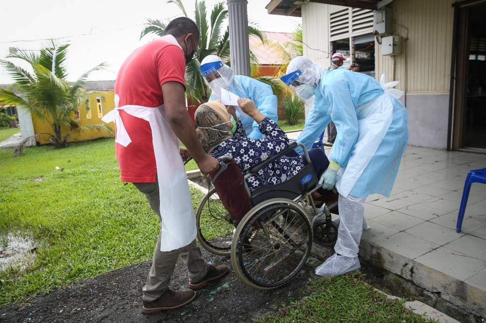 Health workers carry a woman in a wheelchair to be tested for Covid-19 at the Dewan Masyarakat Taman Meru 3 in Klang in this file photo taken on December 2, 2020. — Picture by Yusof Mat Isa