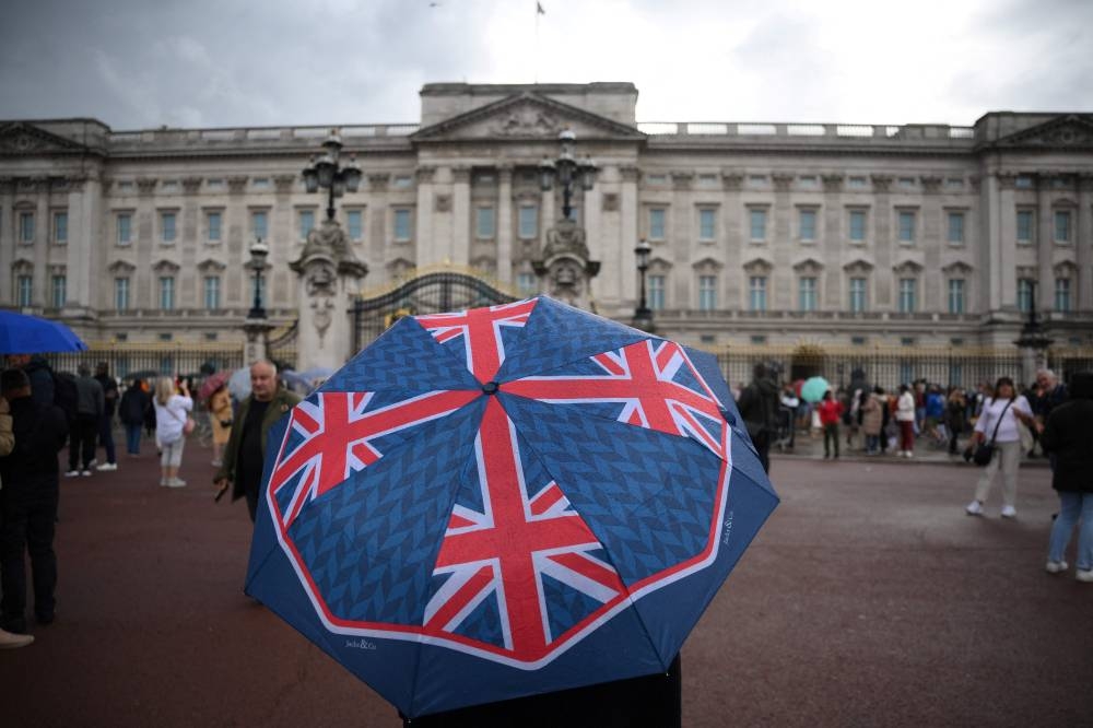 A person with an umbrella picturing the British national flag stands guard in front of Buckingham palace, central London, on September 8, 2022. — AFP pic
