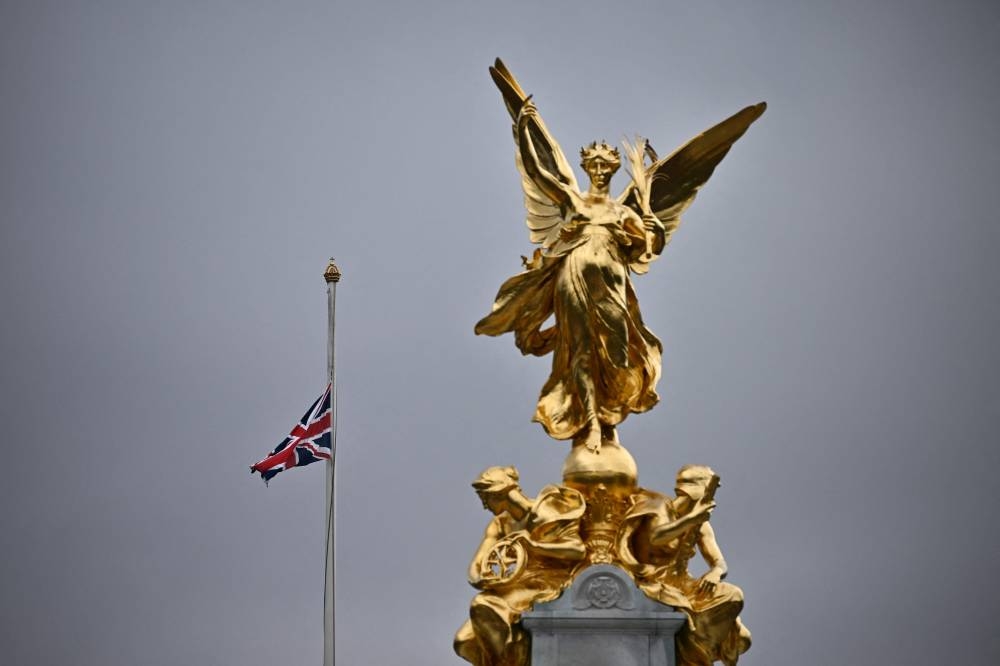 A Union flag flies at half-mast at the top of Buckingham Palace, behind the The Queen Victoria Memorial statue, in London September 9, 2022, as people arrive to gather a day after Queen Elizabeth II died at the age of 96. — AFP pic 